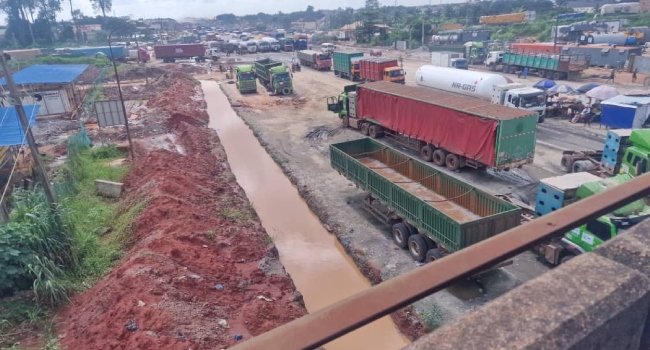 Trucks and vehicles on a damaged section of the Benin-Agbor-Asaba road during federal intervention work
