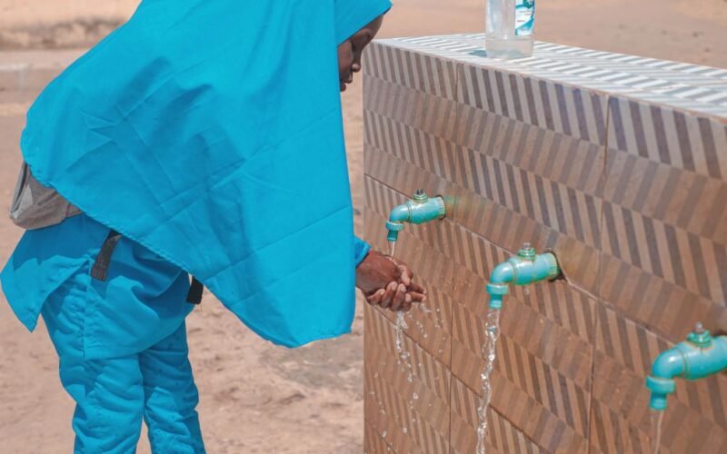 Woman washing her hands at a public water point, illustrating cholera prevention work