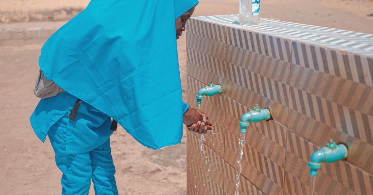 Woman washing her hands at a public water point, illustrating cholera prevention work