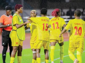 Edo Queens players in yellow kits standing on the pitch during a match.