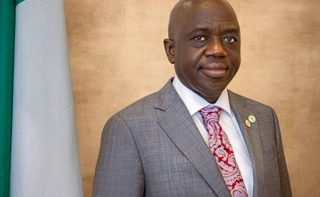 Shamseldeen B. Ogunjimi in a grey suit beside the Nigerian flag