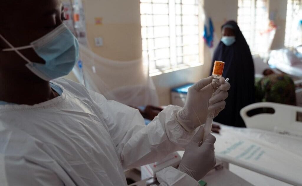 A masked health worker prepares an injection in a clinical setting.