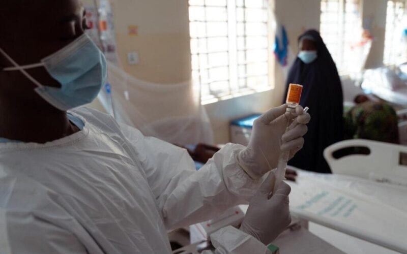 A masked health worker prepares an injection in a clinical setting.