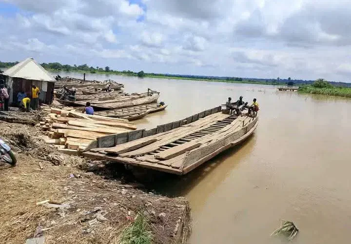 Wooden boats moored beside a muddy riverbank, with people near the landing
