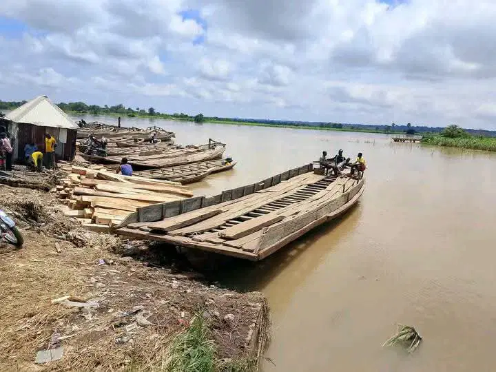 Wooden boats moored beside a muddy riverbank, with people near the landing