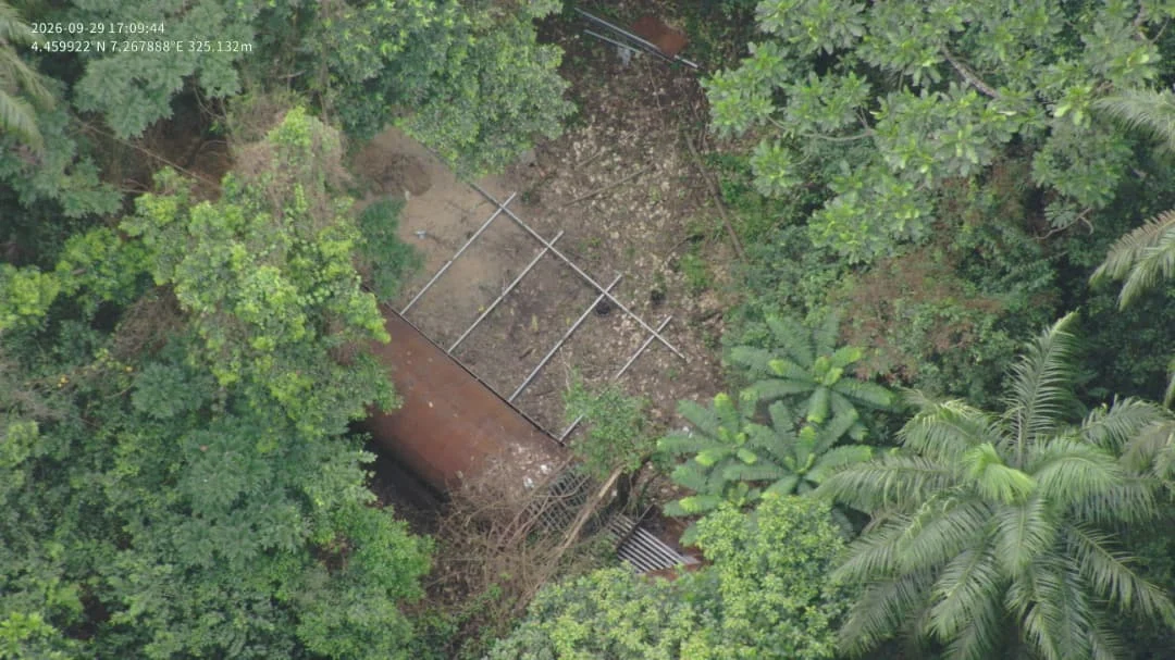 Aerial view of a rust-coloured cylindrical structure and metal framework surrounded by dense vegetation