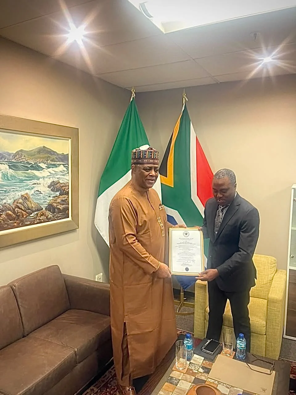 Femi Fani-Kayode, in agbada and cap, presents his credentials to a South African protocol official between the Nigerian and South African flags.