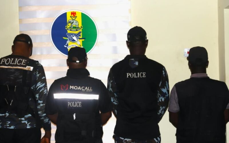 Four men photographed from behind, three wearing police-marked clothing, in front of a police insignia.