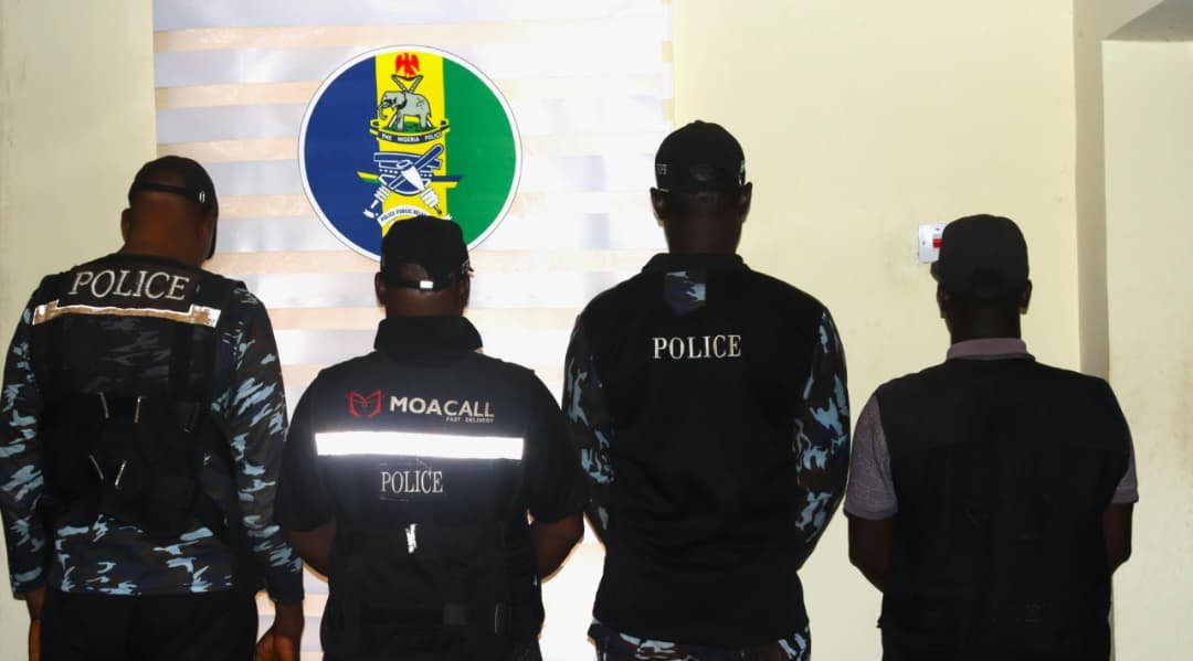 Four men photographed from behind, three wearing police-marked clothing, in front of a police insignia.