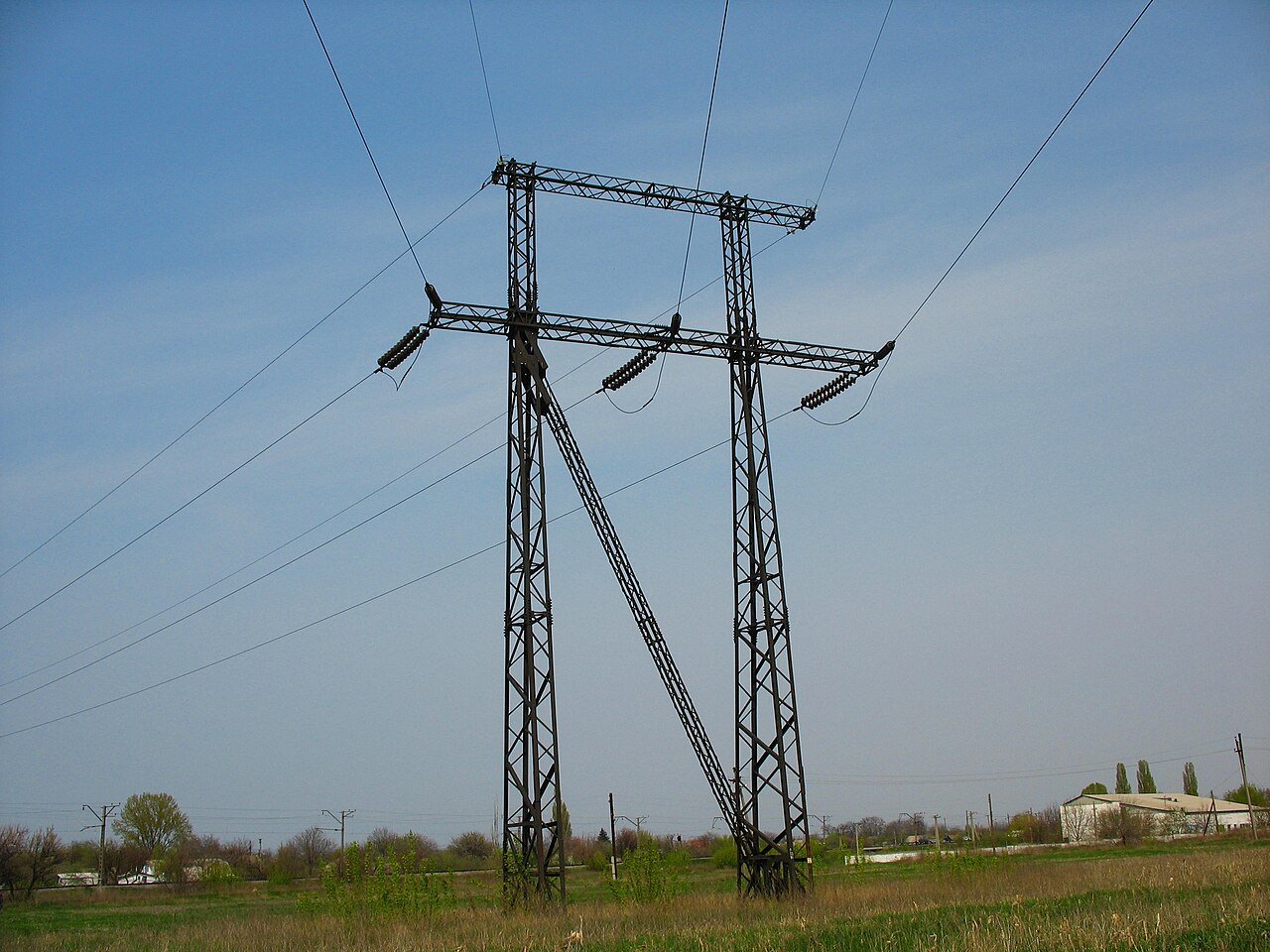 A high-voltage electricity transmission tower carrying overhead power lines over open ground.