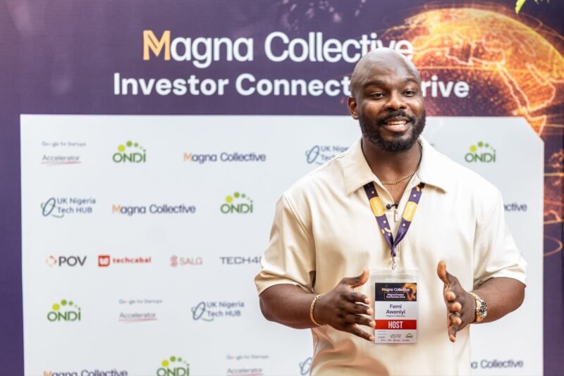 The host of the Magna Investor Connection Drive speaks before a backdrop carrying the event's partner logos.
