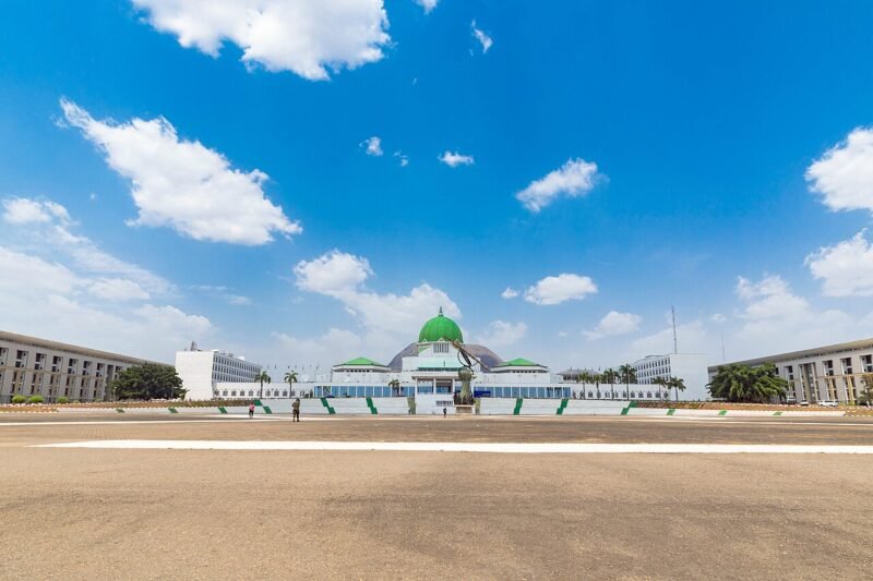 The green-domed main building of the National Assembly complex in Abuja under a clear blue sky.