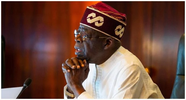 President Bola Tinubu seated beside a microphone with his hands clasped