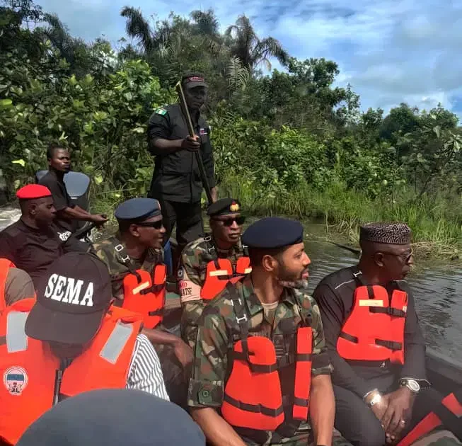 Military and emergency officials wearing life jackets on a boat during a site assessment.