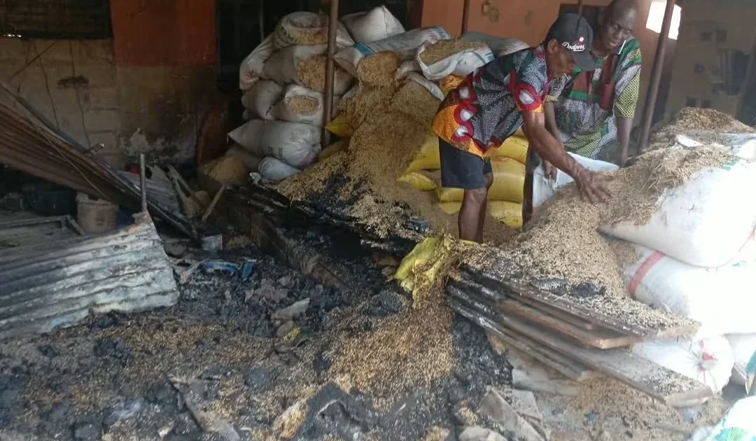 People beside bags of rice and fire-damaged roofing inside a market store