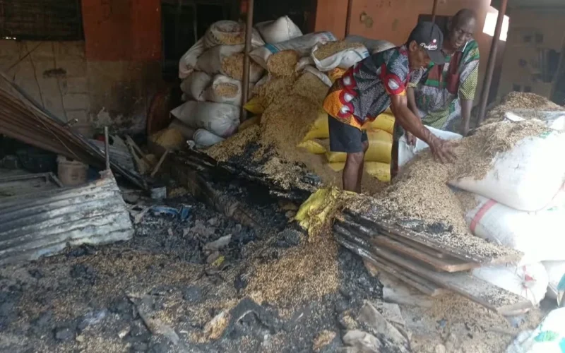 People beside bags of rice and fire-damaged roofing inside a market store
