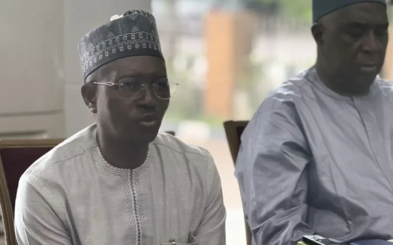 Jonathan Kure seated on the left and speaking at a press conference