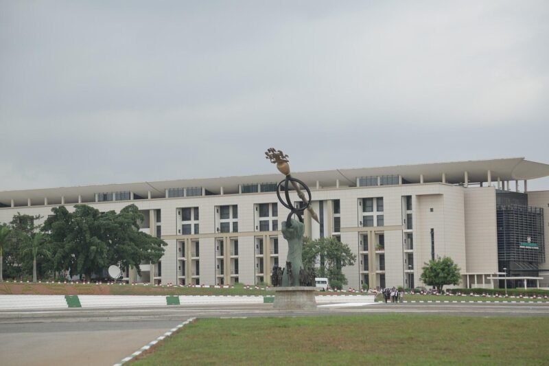 The National Assembly building and a hand holding a ceremonial mace sculpture in Abuja.