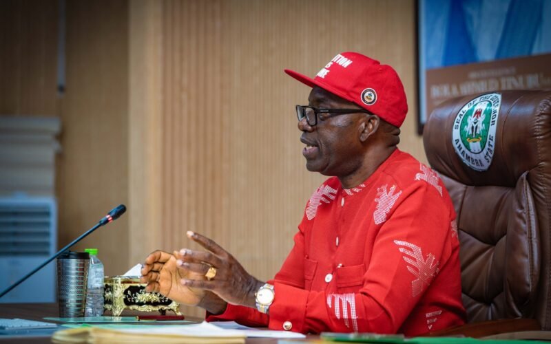 Anambra Governor Charles Soludo seated at a desk wearing a red cap and shirt